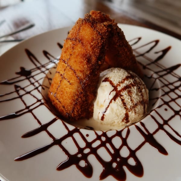 Fried ice cream dessert with two crispy rolls, a scoop of vanilla ice cream, and chocolate drizzle.