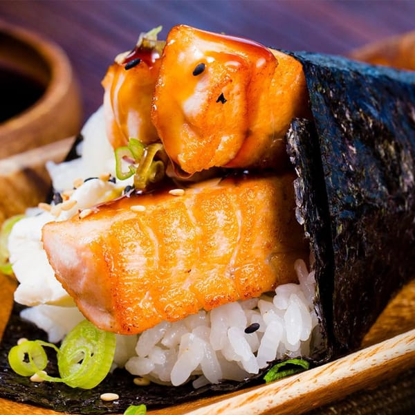 Close-up of a salmon temaki, with rice, green onions, and sesame seeds, on a wooden surface.