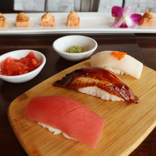 Three pieces of nigiri sushi, pickled ginger, and wasabi on a wooden board.