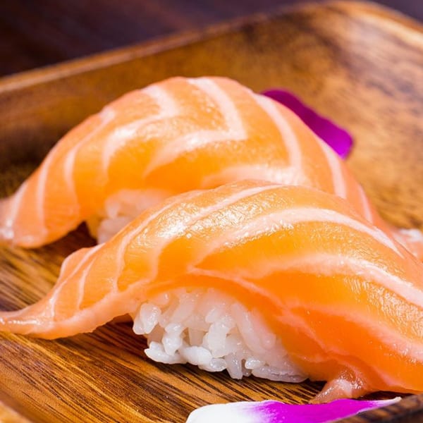 Two pieces of salmon nigiri sushi with purple flower petals on a wooden plate.