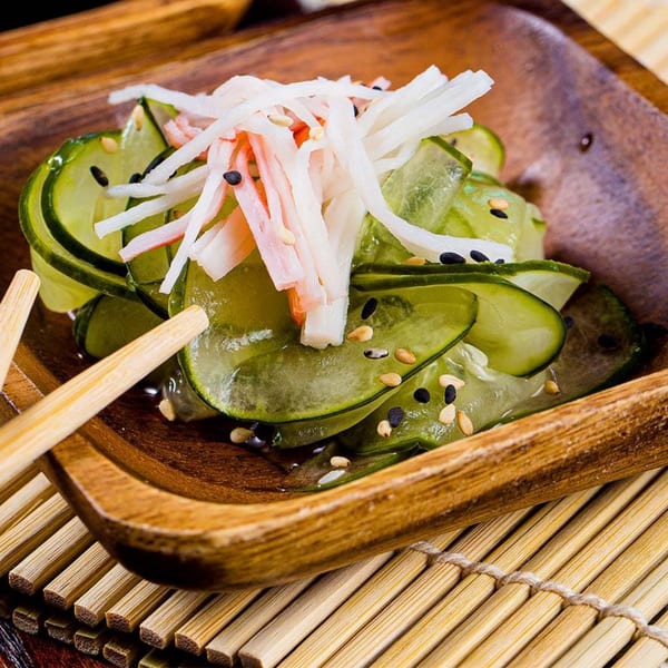 Cucumber salad with imitation crab, sesame seeds, and chopsticks in a wooden bowl.