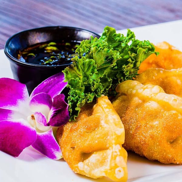 Golden-fried wontons with a side of dark dipping sauce, garnished with lettuce and an orchid.