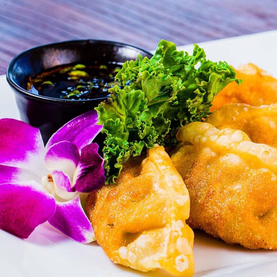 Golden-fried wontons with a side of dark dipping sauce, garnished with lettuce and an orchid.