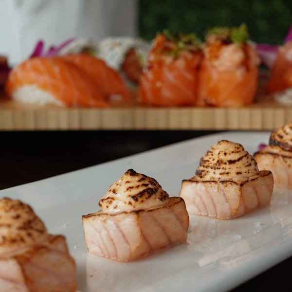 Seared salmon sushi with creamy topping and other sushi rolls on a wooden board.