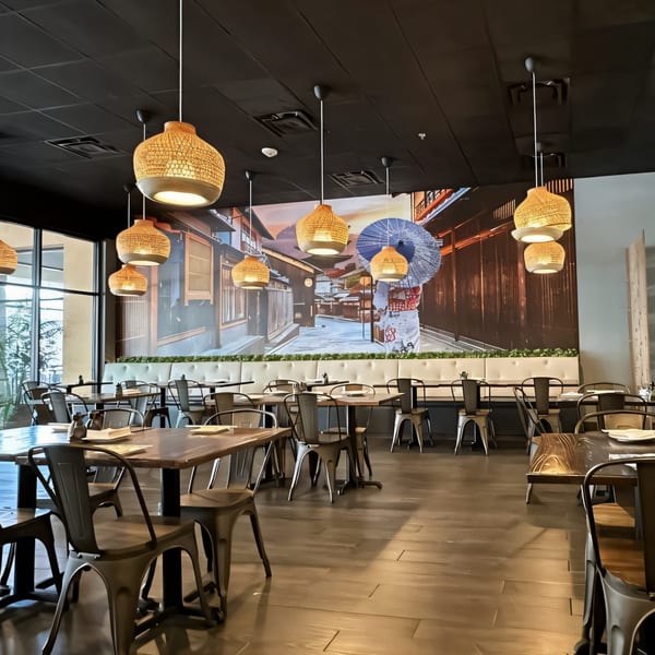 Modern restaurant interior with dark tables, metal chairs, and a large Japanese street mural.