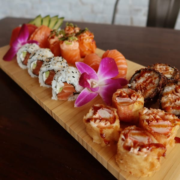 A wooden board filled with various sushi rolls, sashimi, and nigiri, garnished with purple orchids.