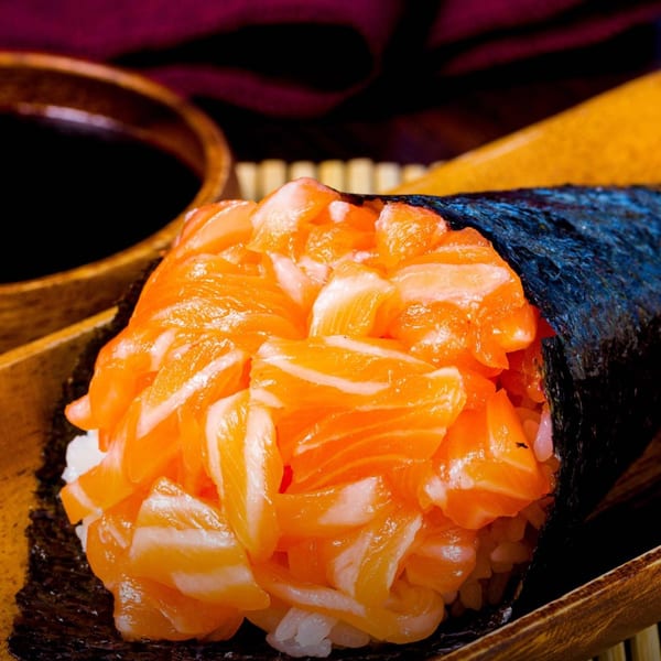 Close-up of a salmon temaki hand roll with rice and nori, served with soy sauce.