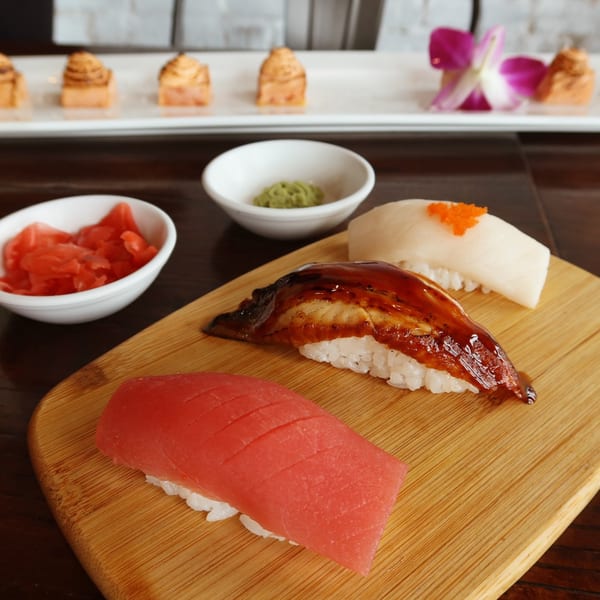 Three pieces of nigiri sushi on a wooden board with ginger and wasabi.