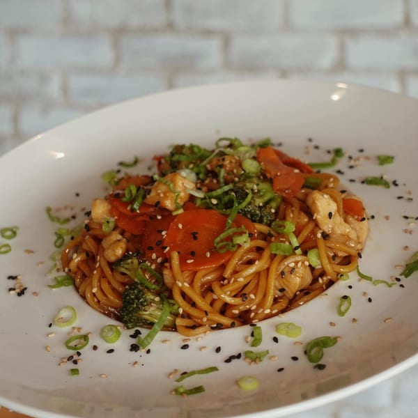 Chicken lo mein with broccoli, carrots, and scallions, garnished with sesame seeds on a white plate.