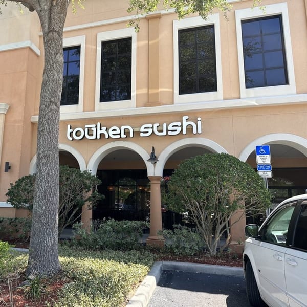 Exterior view of Touken Sushi restaurant with arched entrance, landscaping, and a white car.