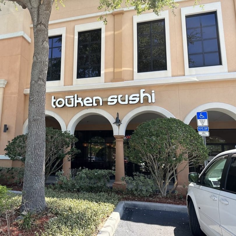 Exterior view of Touken Sushi restaurant with arched entrance, landscaping, and a white car.