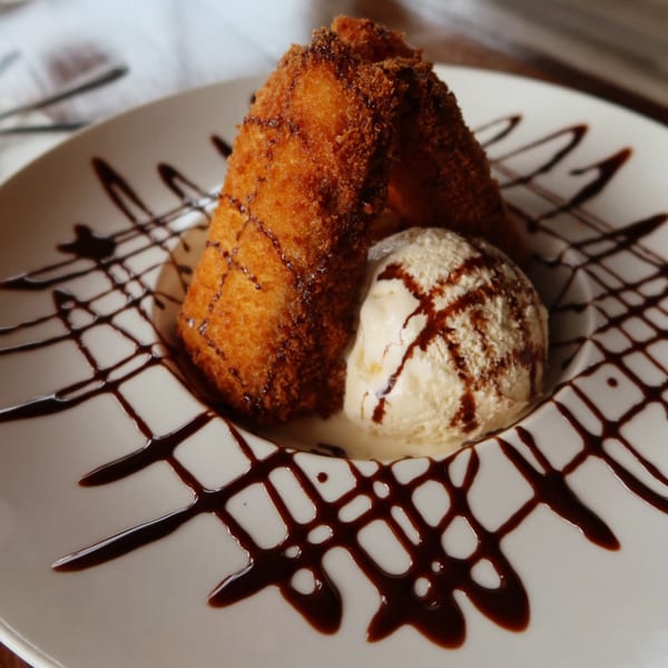 Two golden-fried dessert pieces with a scoop of vanilla ice cream, drizzled with chocolate sauce.