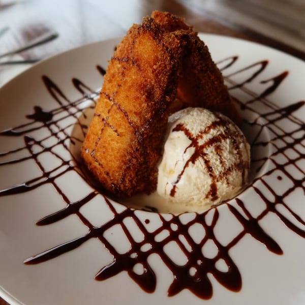 Fried banana dessert with vanilla ice cream and chocolate drizzle on a white plate.