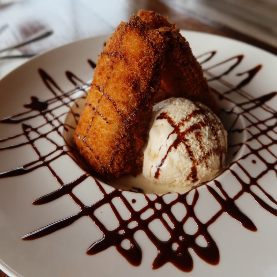 Fried banana dessert with vanilla ice cream and chocolate drizzle on a white plate.